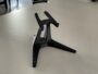 Schwarz 3D-gedruckter Ständer mit dreibeinigem Fuß und zwei nach vorn gebogenen Haltekrallen, auf einer hellgrauen Tischplatte.