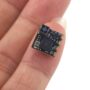 Winzige rechteckige Leiterplatten-Baugruppe mit schwarzem Mikrochip, mehreren SMD-Bauteilen und goldenen Kontaktlötflächen, auf der Fingerspitze einer Hand gehalten.