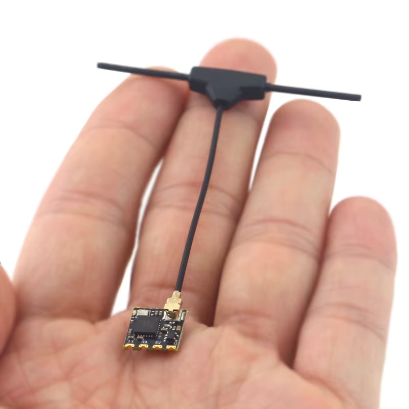 Hand nahe fotografiert, die eine winzige schwarze Leiterplatte mit goldfarbenen Kontakten und einem dünnen schwarzen Kabel hält, das zu einer T-förmigen Stabantenne führt