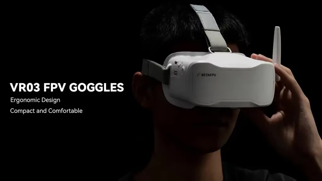 Produktfoto mit weißen VR03 FPV-Goggles der Marke BETAFPV, getragen von einer Person vor schwarzem Hintergrund; rechts die Brille mit Kopfband und Antenne, links sichtbare weiße Werbetexte VR03 FPV GOGGLES, Ergonomic Design, Compact and Comfortable.