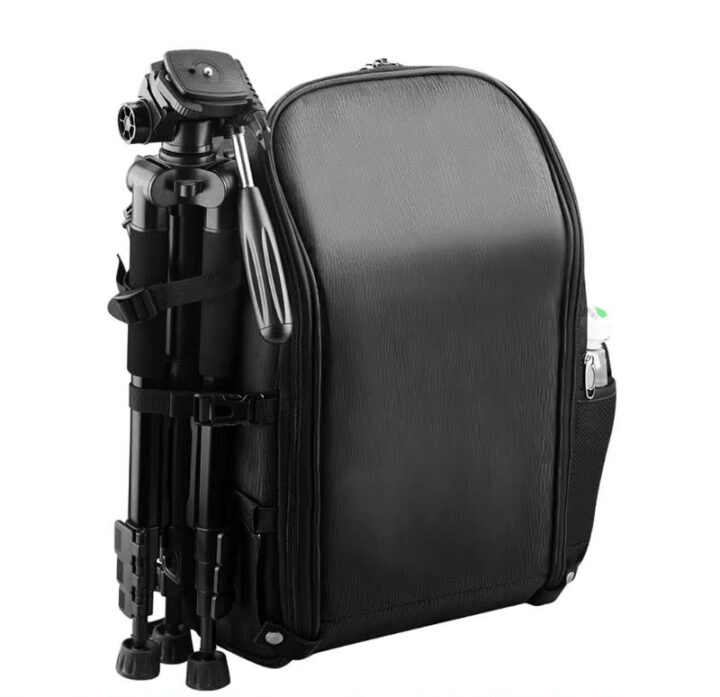 fpv-drohnen-rucksack-aufbewahrung-akku-funksender Schwarzer kompakter Kamerarucksack mit glatter, feinstrukturierter Front, an dessen linker Seite ein zusammengeklapptes Kamerastativ mit Panhandle befestigt ist und in der seitlichen Netztasche eine Wasserflasche steckt.