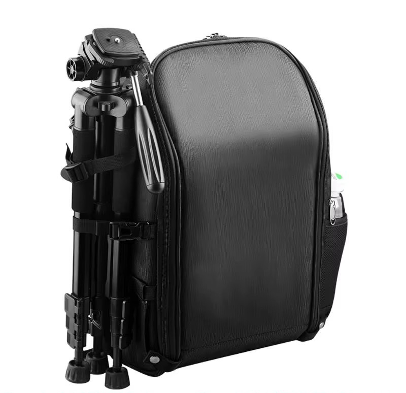 fpv-drohnen-rucksack-aufbewahrung-akku-funksender Schwarzer kompakter Kamerarucksack mit glatter, feinstrukturierter Front, an dessen linker Seite ein zusammengeklapptes Kamerastativ mit Panhandle befestigt ist und in der seitlichen Netztasche eine Wasserflasche steckt.