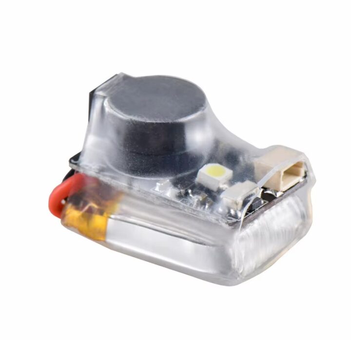 fpv-finder-buzzer-mit-ladeanzeige-und-reset-taste Kleines, transparent umhülltes Elektronikmodul mit rundem schwarzen Bauteil, einer SMD-LED, weißem Steckkontakt und roter Anschlussleitung auf weißem Hintergrund.
