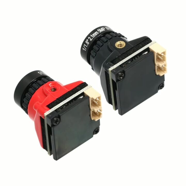 fpv-kamera-mit-osd-und-umstellbarem-bildformat Zwei kleine Board-Kameras mit sichtbaren Objektiven—eine mit rotem, eine mit schwarzem Gehäuse—jeweils mit schwarzer Frontabdeckung, goldfarbenem Gewindeanschluss und beige Mehrfachstecker auf weißem Hintergrund.