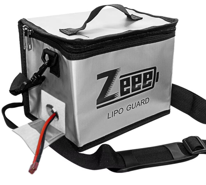 fpv-lipo-akku-aufbewahrung-tasche-feuerfest Silberne rechteckige LiPo-Sicherheitsbox mit Reißverschluss, Tragegriff und abnehmbarem Schultergurt, Vorderseite mit Schriftzug „Zeep LIPO GUARD“ und ein rot-schwarzes Batteriekabel, das durch eine seitliche Öffnung führt.