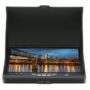 Klappbarer schwarzer LCD-Monitor mit Sonnenblende und Bedientasten, auf dem eine beleuchtete Stadt mit einer Fußgängerbrücke und ihren Lichterspiegelungen im Wasser bei Abenddämmerung zu sehen ist.