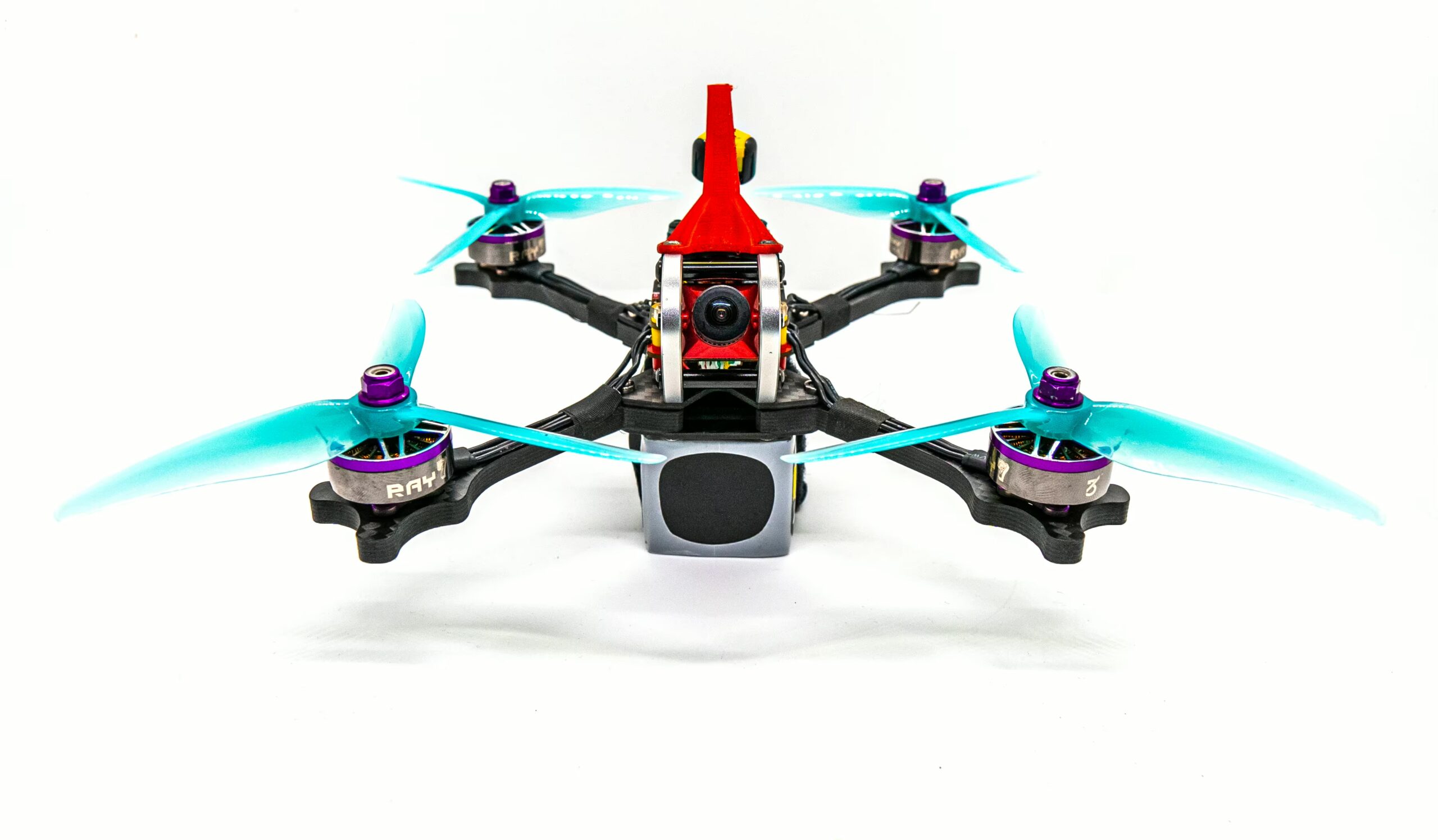 fpv-propeller-gemfan-51466-v2-5-zoll-dreiblatt FPV‑Racing‑Drohne mit vier türkisblauen 5‑Zoll‑Dreiblatt‑Propellern, roter Haube, nach vorn gerichteter Kamera und schwarzem Carbon‑Rahmen vor weißem Hintergrund.