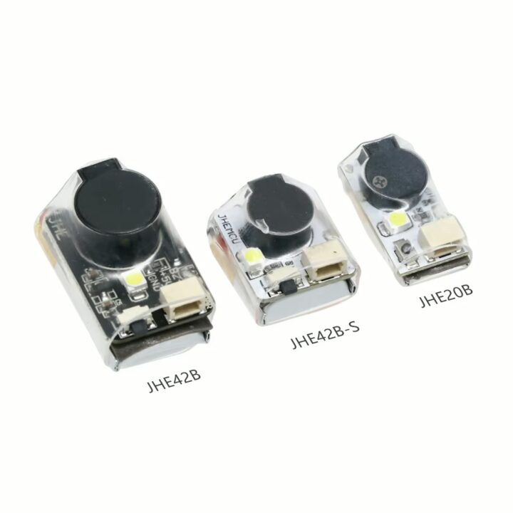 fpv-racing-drone-buzzer-mit-led-summeralarm Drei kompakte transparente Elektronikmodule (beschriftet JHE42B, JHE42B‑S und JHE20B) mit rundem schwarzem Piezo‑Element, kleiner LED und Anschlussbuchse auf weißem Hintergrund.