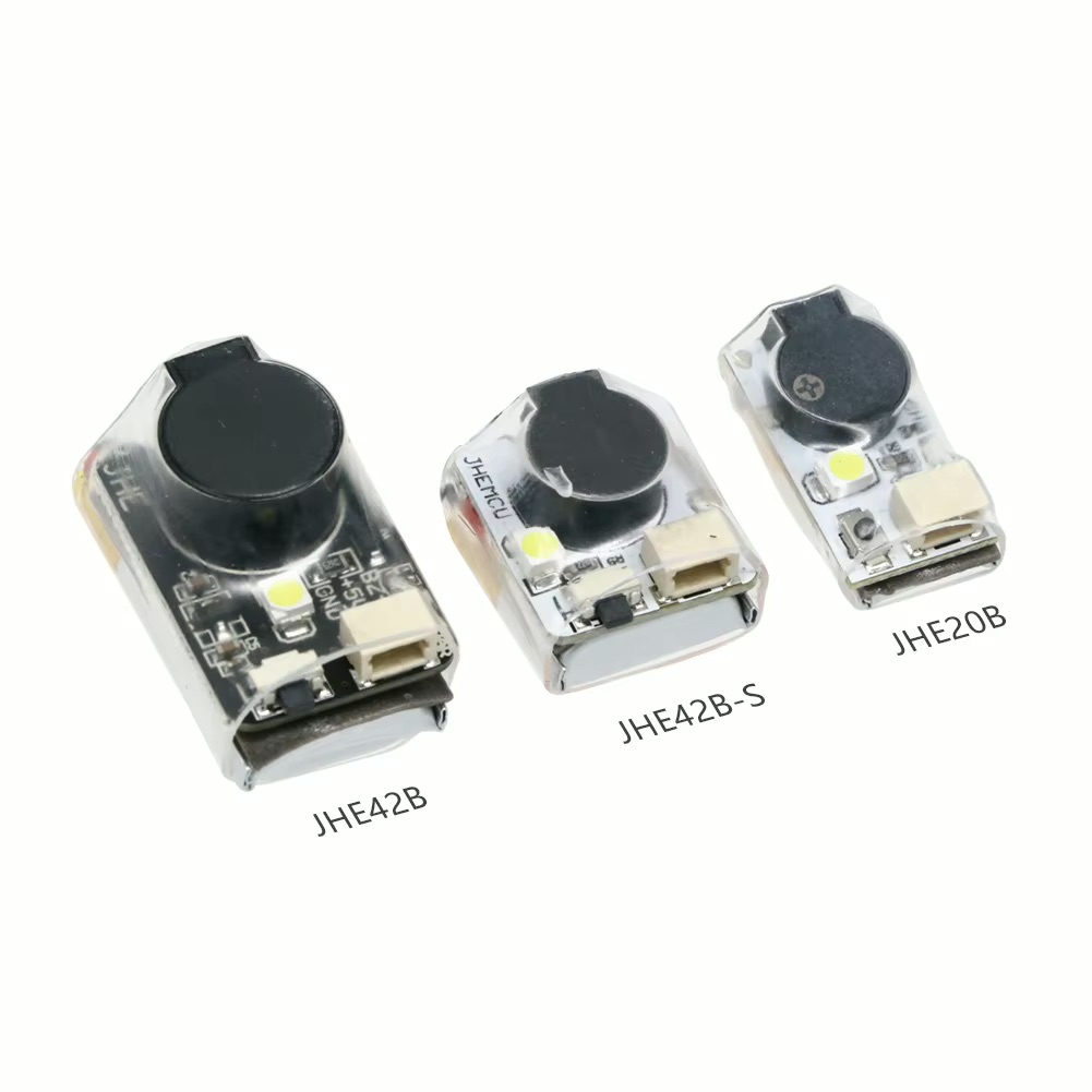 Drei kompakte transparente Elektronikmodule (beschriftet JHE42B, JHE42B‑S und JHE20B) mit rundem schwarzem Piezo‑Element, kleiner LED und Anschlussbuchse auf weißem Hintergrund.