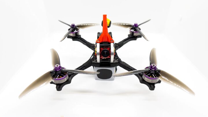 fpv-racing-drone-propeller-gemfan-51466 Frontansicht einer FPV-Renn-Drohne auf weißem Hintergrund mit roter Cockpit-Verkleidung, sichtbarer Kamera, vier Carbon-Armen und vier 5-Zoll-Dreiblatt-Propellern mit lila Motorhauben.