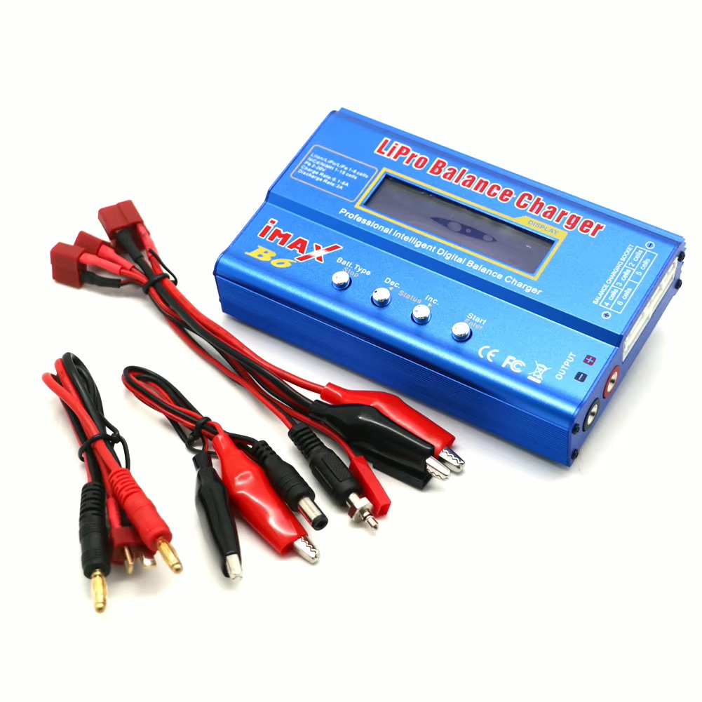 Blaues iMax B6 LiPo-Balance-Ladegerät mit LCD-Display und vier Bedienknöpfen, dazu mehrere rote und schwarze Anschlusskabel, Krokodilklemmen und Stecker auf weißem Hintergrund.