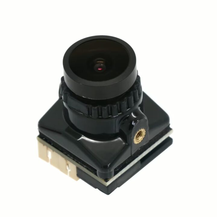 kompakte-fpv-kamera-fuer-freestyle-und-racing Kleine schwarze Boardkamera mit rundem Weitwinkelobjektiv und geriffeltem Fokusring, glänzender Kunststoffabdeckung, goldfarbenem Gewindeeinsatz und weißem Steckverbinder auf quadratischer Platine vor weißem Hintergrund.