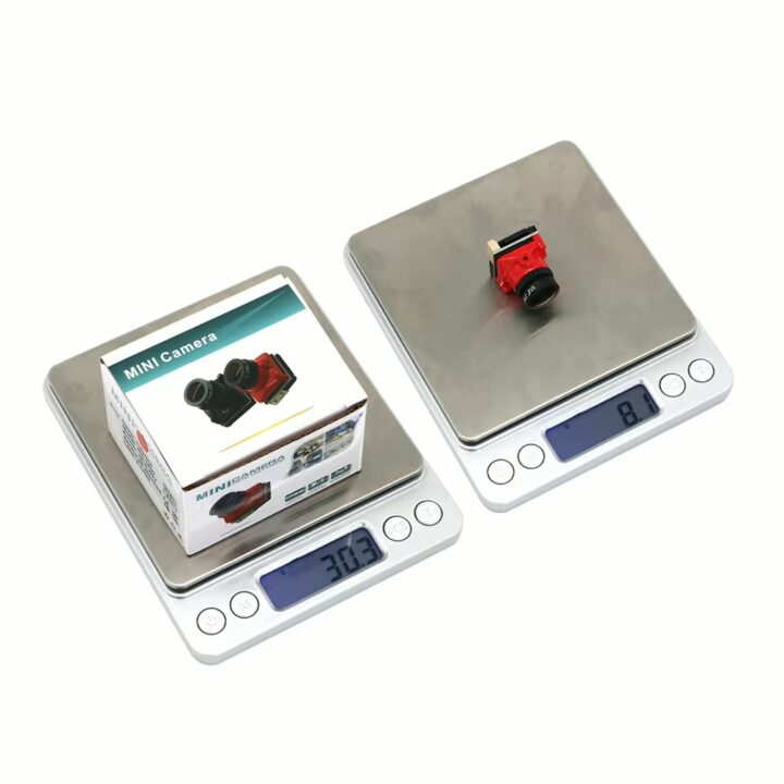 leichte-fpv-hd-kamera-fuer-fpv-racing-builds Zwei digitale Waagen mit Edelstahlwiegeflächen: links steht eine verpackte 'MINI Camera' auf der Waage (Display 30,3 g), rechts liegt eine kleine rote Kamerabaugruppe auf der Waage (Display 8,1 g), beide mit blau hintergrundbeleuchteten LCD-Anzeigen.