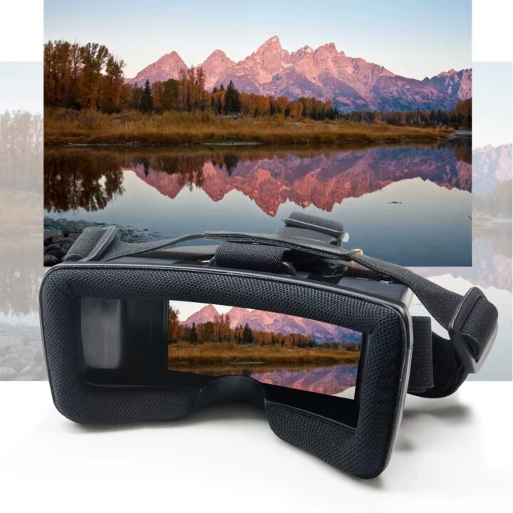 VR-Brille mit gepolstertem Rahmen und verstellbarem Kopfband im Vordergrund, deren Linsen eine herbstliche Berglandschaft mit rosa beleuchteten Gipfeln und spiegelglattem See samt Uferbäumen reflektieren.