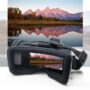 VR-Brille mit gepolstertem Rahmen und verstellbarem Kopfband im Vordergrund, deren Linsen eine herbstliche Berglandschaft mit rosa beleuchteten Gipfeln und spiegelglattem See samt Uferbäumen reflektieren.