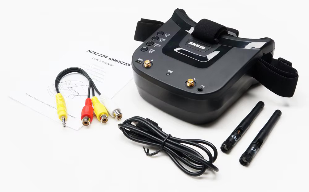 Schwarze FPV-Drohnenbrille mit gepolstertem Kopfband, zwei 5,8‑GHz-Antennen, AV‑/RCA‑Kabeln und Bedienungsanleitung auf weißem Hintergrund.